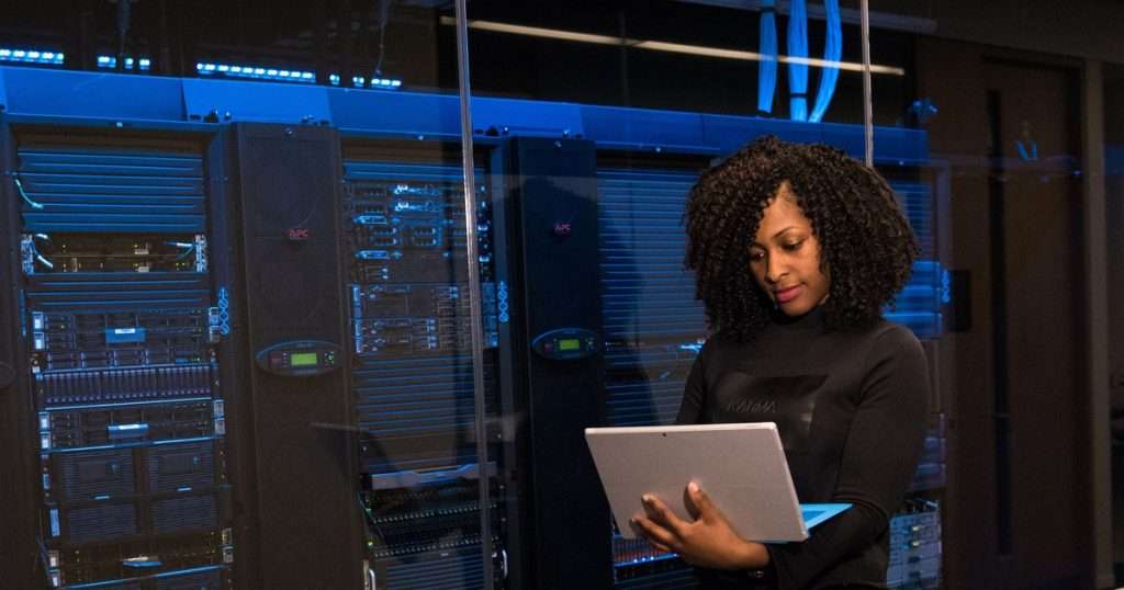 Administradora de TI consulta una tableta frente a los bastidores de una sala de servidores, el tipo de operación que se protege con Azure Site Recovery