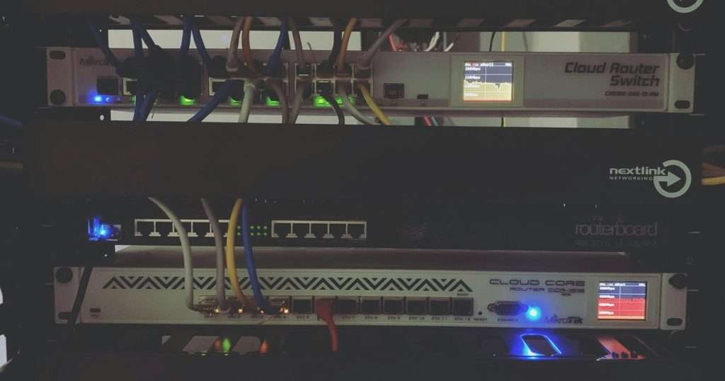 MikroTik en un rack de red: un Cloud Router Switch, un RouterBOARD RB3011 y un Cloud Core Router en funcionamiento, con cables y pantallas de tráfico