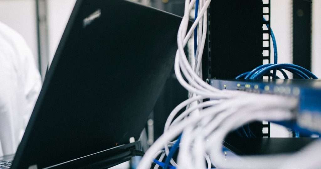 Técnico con un portátil abierto junto a un rack de red con un switch y su cableado, el escenario habitual para instalar y configurar OPNsense
