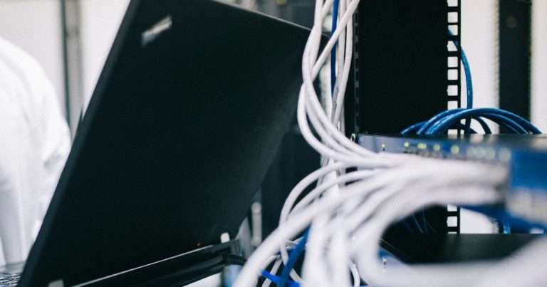 Técnico con un portátil abierto junto a un rack de red con un switch y su cableado, el escenario habitual para instalar y configurar OPNsense