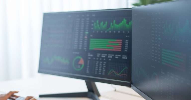 Dos monitores con un tablero de monitoreo de red del tipo que ofrece PRTG Network Monitor: gráficas, barras de estado en verde y rojo y un indicador circular