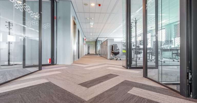 Canales de Teams: pasillo de oficina con salas de paredes de vidrio a ambos lados, cada una con su propio espacio de trabajo dentro de la misma planta