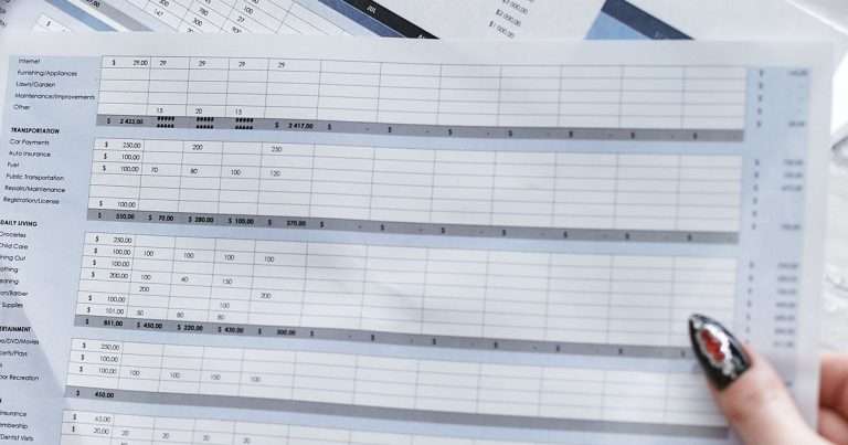Combinar celdas en Excel: una hoja de cálculo impresa con grupos de filas, filas de totales que cruzan varias columnas y una mano que la sostiene