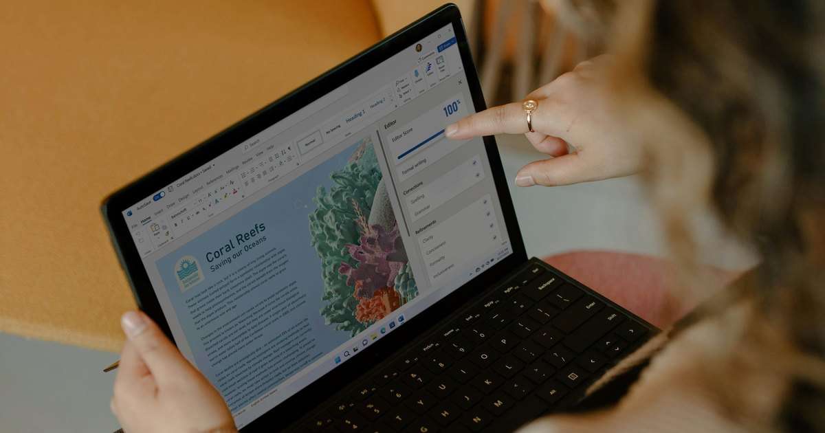 Compartir archivos en OneDrive: una persona sostiene un portátil Surface con un documento de Word abierto, con el Autoguardado activado y el botón para compartir arriba a la derecha, y señala la pantalla