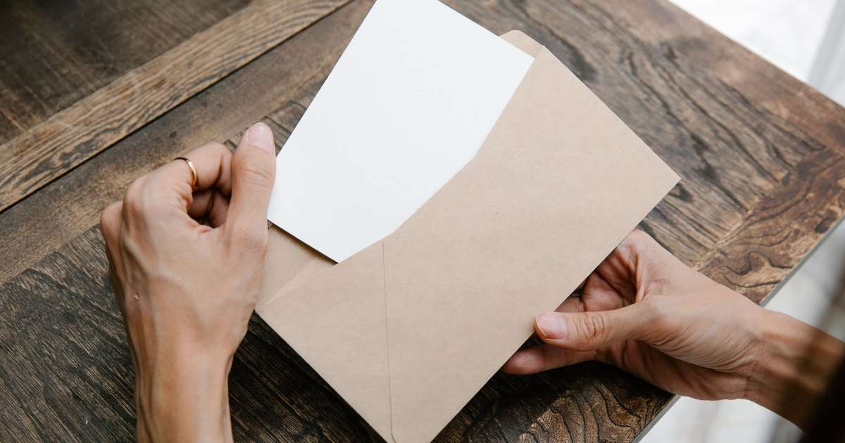 Confirmación de lectura en Outlook: dos manos sacan una tarjeta en blanco de un sobre de papel kraft sobre un escritorio de madera