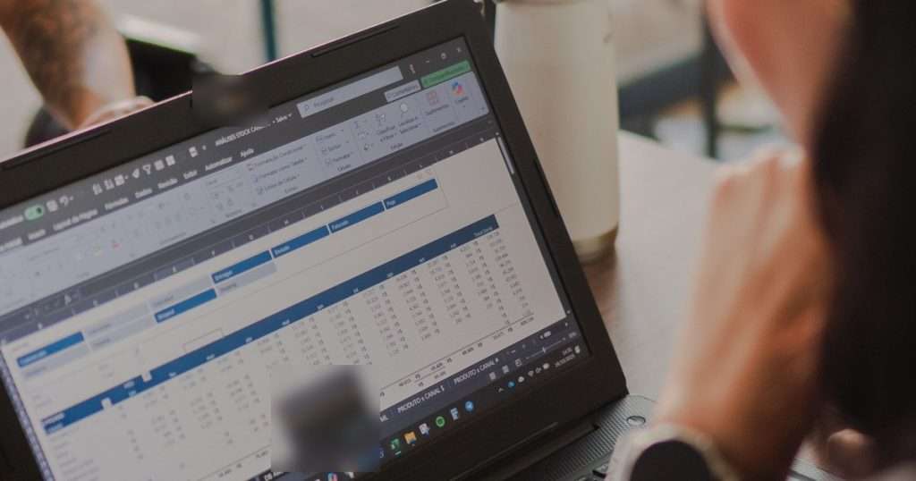 Excel avanzado: portátil con una hoja de cálculo de Excel abierta, con la cinta de opciones y un resumen de cifras por mes, mientras una persona la revisa