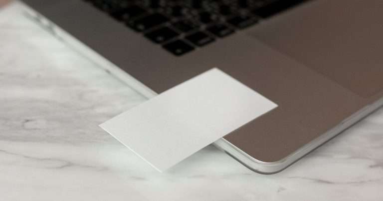 Firma en Gmail: tarjeta de presentación en blanco apoyada sobre un portátil abierto, encima de una mesa de mármol