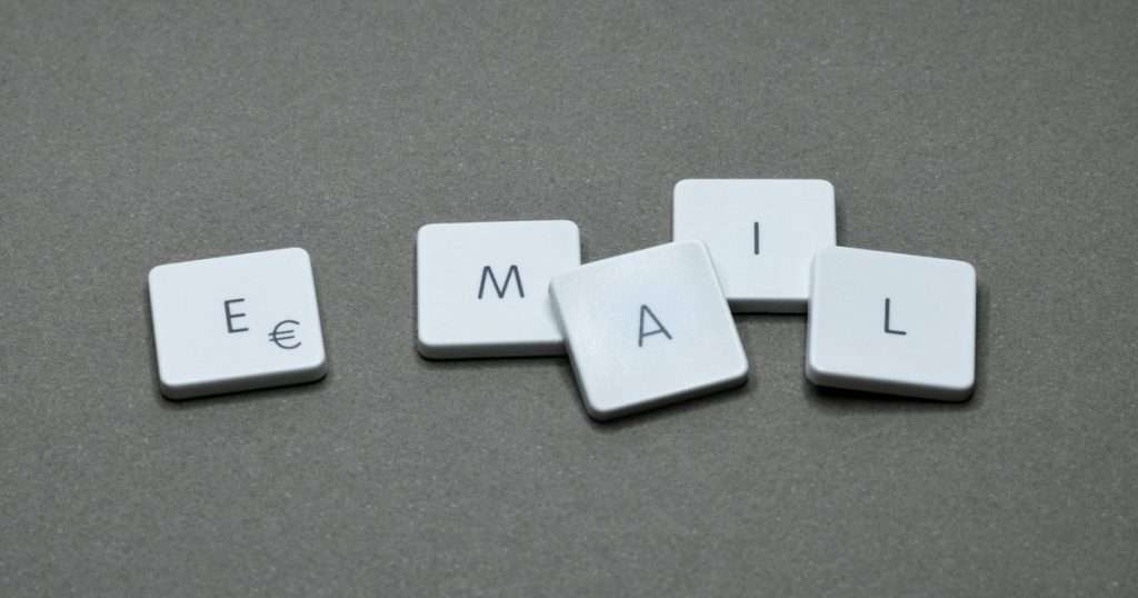Firma en Outlook: cinco teclas blancas sueltas forman la palabra email sobre un fondo gris, como el texto que se repite al pie de cada correo