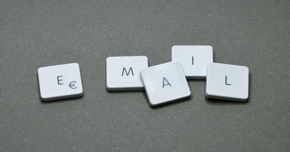 Firma en Outlook: cinco teclas blancas sueltas forman la palabra email sobre un fondo gris, como el texto que se repite al pie de cada correo