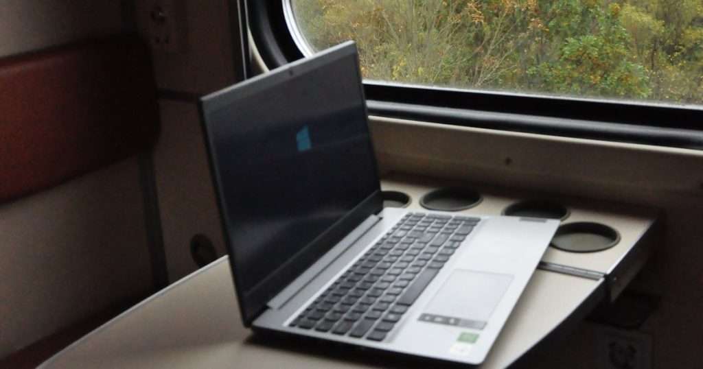 Google Drive para escritorio: portátil con Windows abierto sobre la mesa plegable de un tren, junto a una ventana con árboles