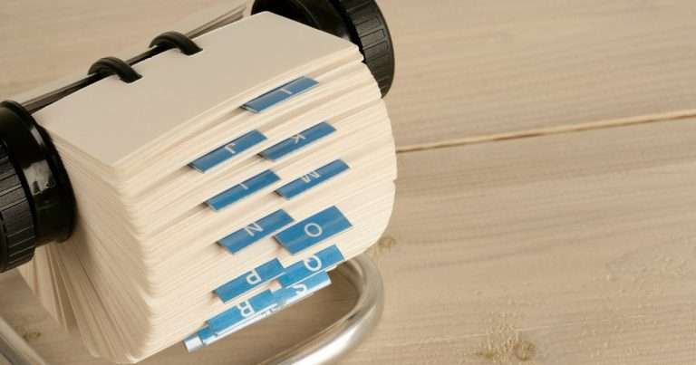 Grupo de contactos en Outlook: tarjetero giratorio de direcciones con pestañas alfabéticas azules sobre un escritorio de madera clara