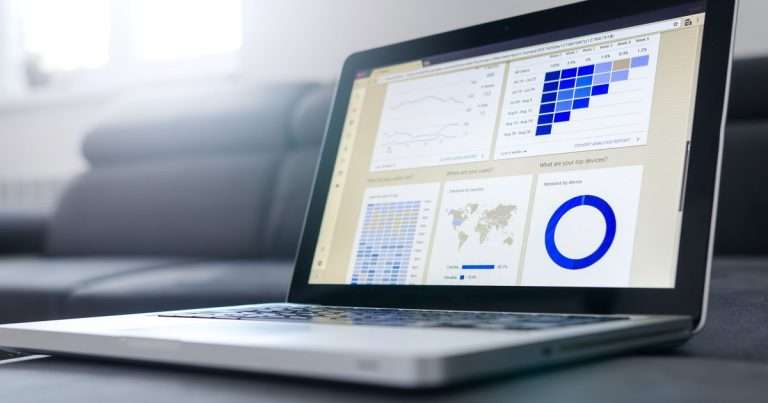 Power BI básico: portátil sobre un sofá con un tablero de datos en pantalla, formado por gráficos de líneas, una tabla de colores, un mapa y un gráfico de anillo