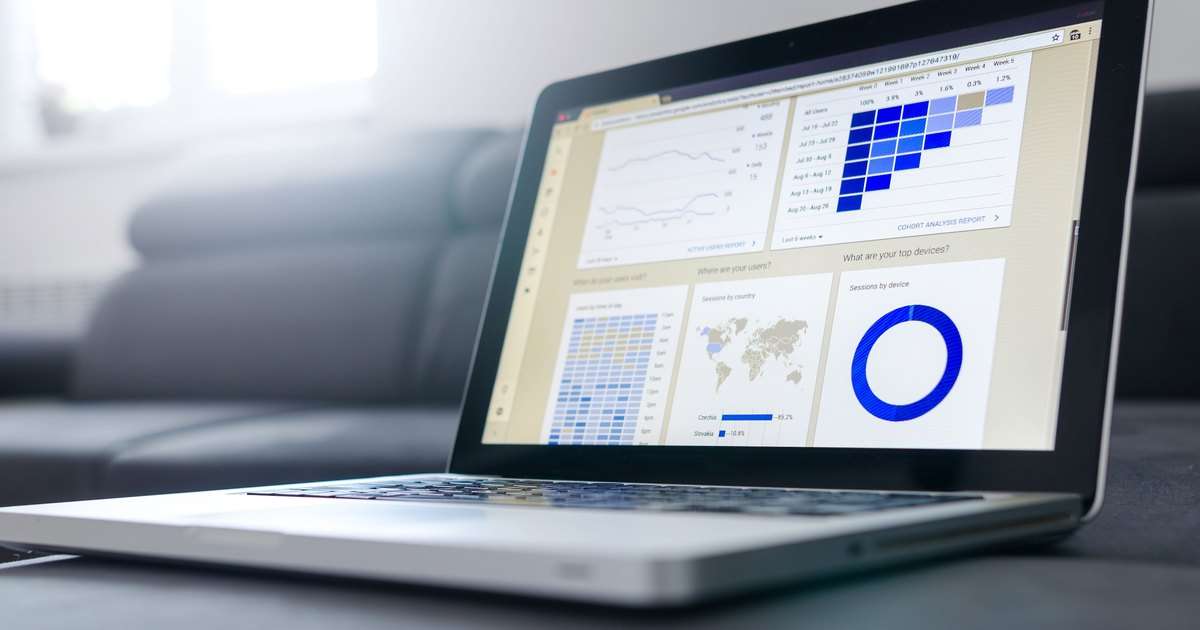 Power BI básico: portátil sobre un sofá con un tablero de datos en pantalla, formado por gráficos de líneas, una tabla de colores, un mapa y un gráfico de anillo