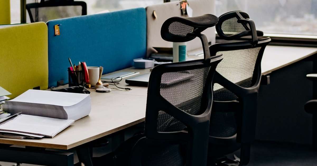 Respuesta automática en Outlook: dos sillas de oficina vacías junto a un escritorio con papeles, un portalápices y una taza, en un puesto de trabajo sin nadie