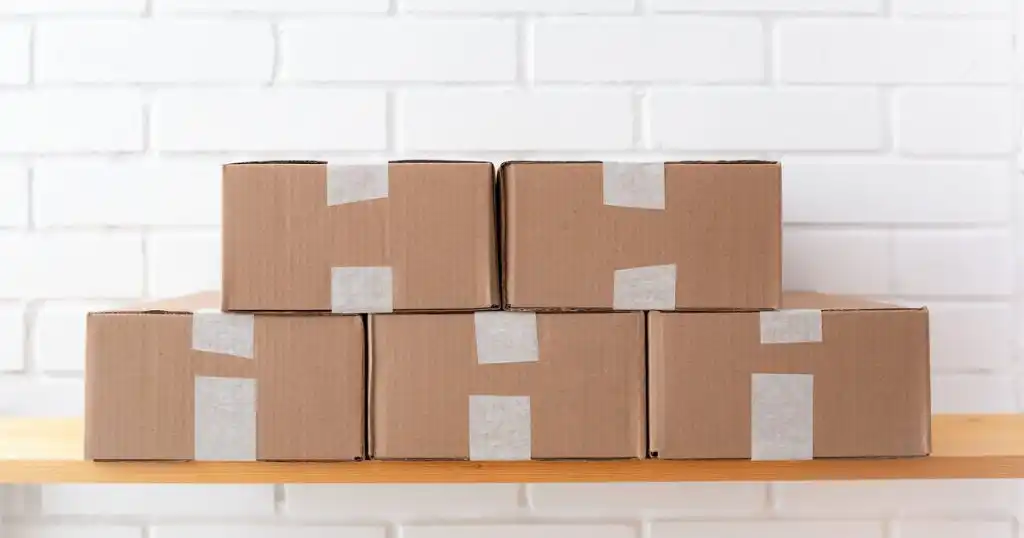 Winget, el administrador de paquetes de Windows: cinco cajas de cartón iguales, cerradas con cinta, ordenadas sobre una repisa de madera frente a una pared de ladrillo blanco